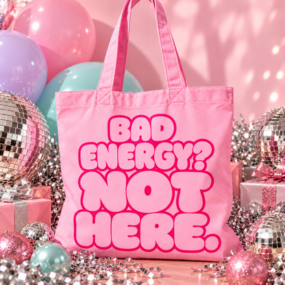Pink organic cotton tote bag with “Bad Energy? Not Here.” bubble lettering, photographed with silver disco balls and Christmas decorations.
