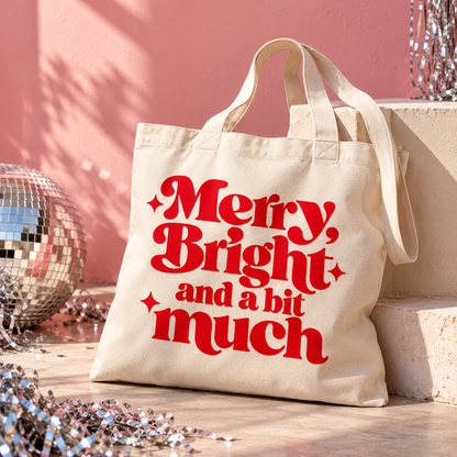Natural organic cotton Christmas tote bag with bold red “Merry, Bright and a bit much” lettering and three decorative sparkles.