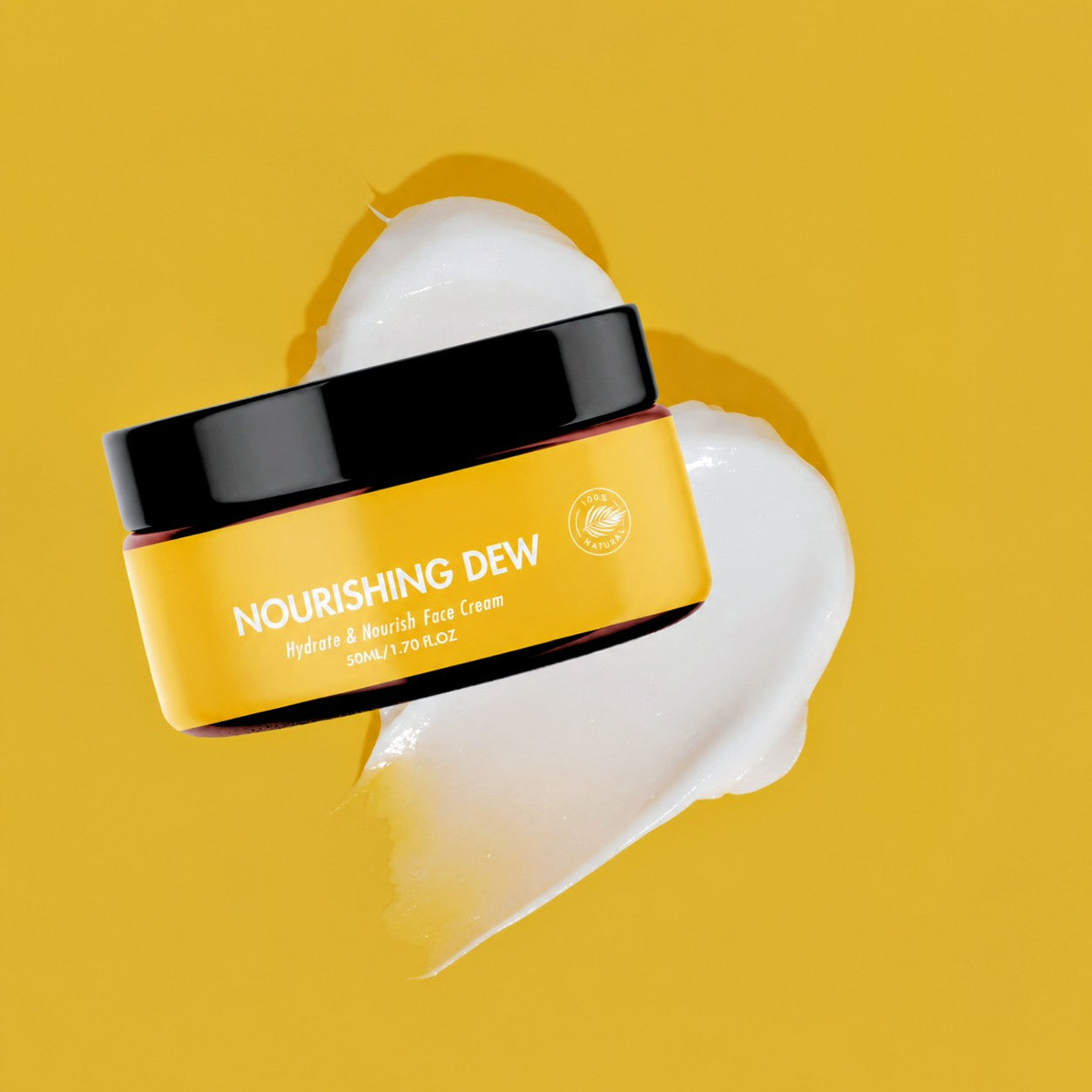 A jar of Nourishing Dew Hydrating & Enriching Face Cream shown on a bright yellow background with a smear of white cream behind it.