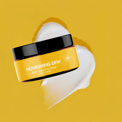 A jar of Nourishing Dew Hydrating & Enriching Face Cream shown on a bright yellow background with a smear of white cream behind it.