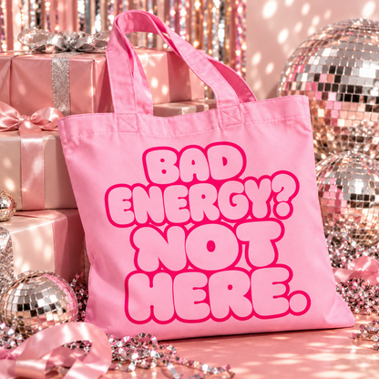 Pink organic cotton tote bag with “Bad Energy? Not Here.” bubble lettering, photographed with silver disco balls and Christmas decorations.
