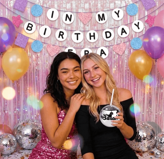 "Two girls posing in front of a pink iridescent foil curtain backdrop with silver disco ball cups."