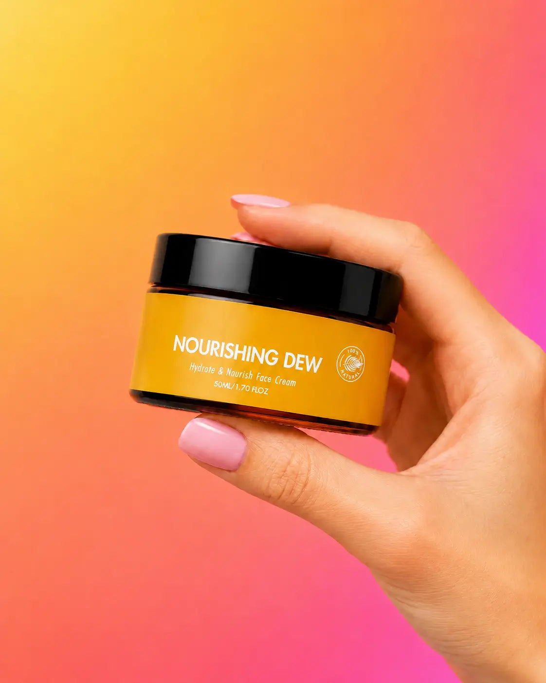 A hand with pink manicured nails holds a jar of Nourishing Dew Water & French Tan Cream against a vibrant yellow-to-pink gradient background.